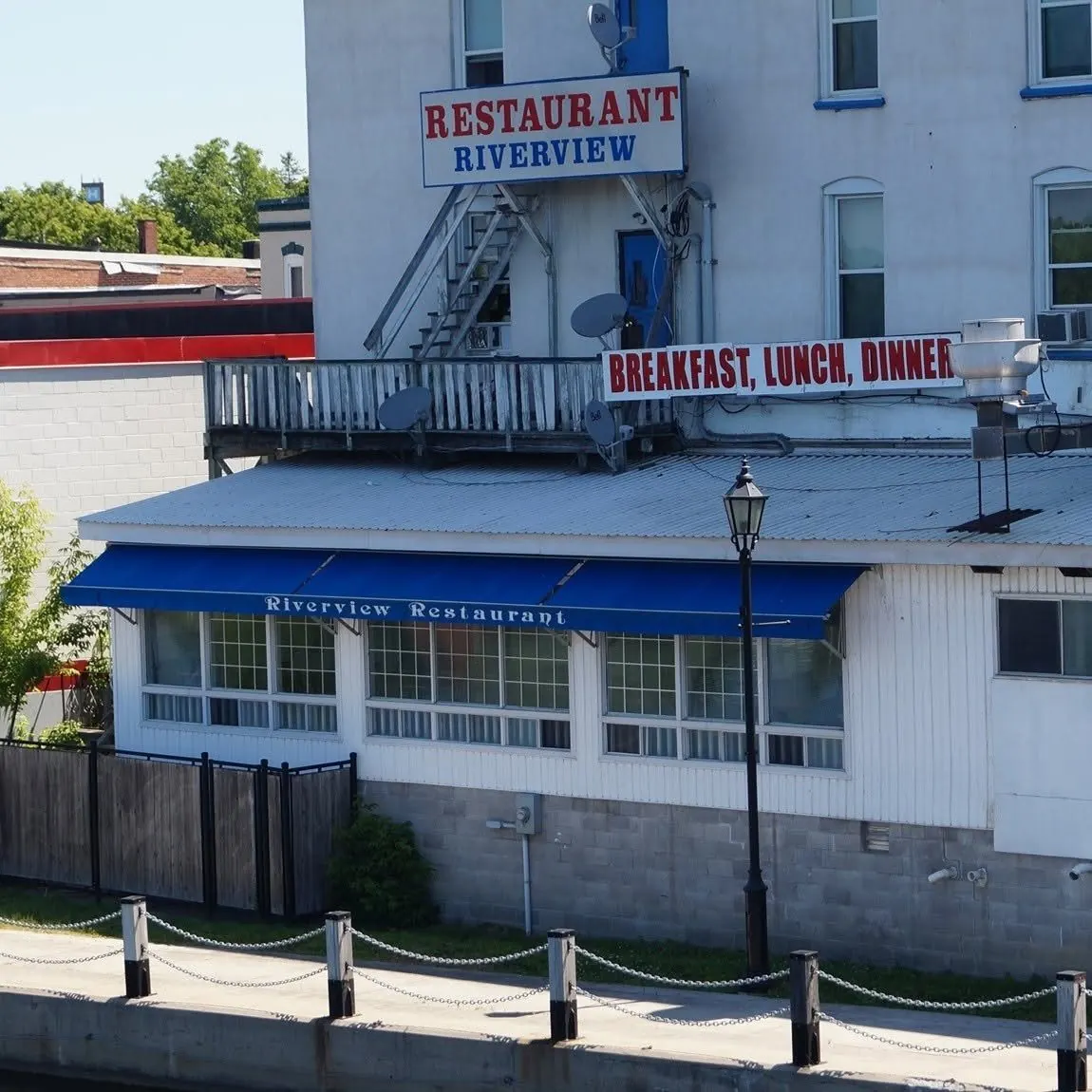 The river side of the Riverview, with its blue awning and Breakfast, Lunch, Dinner sign, seen from the riverwalk